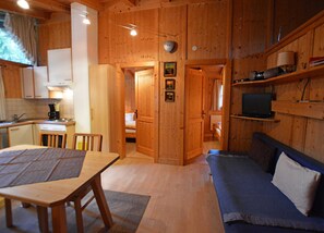 Interior de una cabaña de madera con una mesa de comedor, un sofá, una cocina y un televisor.