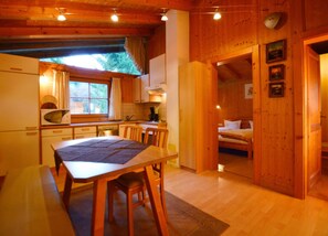 Interior de una cabaña de madera con comedor, cocina y un dormitorio con cama.