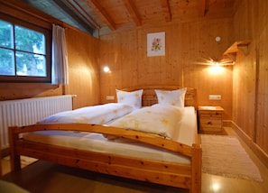 Un dormitorio con paneles de madera, una cama, mesitas de noche, un radiador y una ventana.