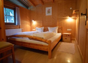 Un dormitorio con paneles de madera, una cama, mesitas de noche, una silla y un ventanal.