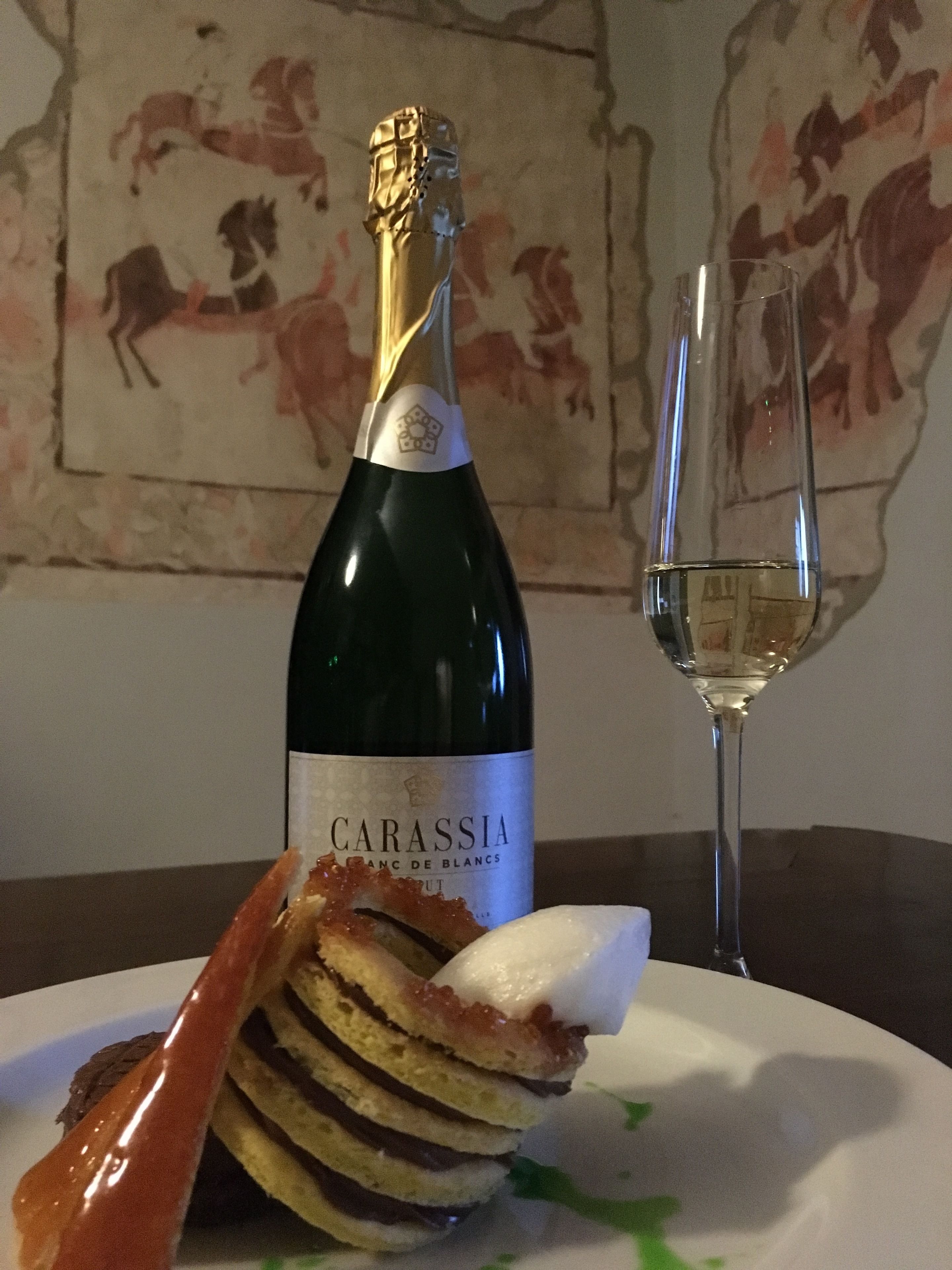 A bottle of Carassia wine, a glass of white wine, and a plate with a layered dessert.