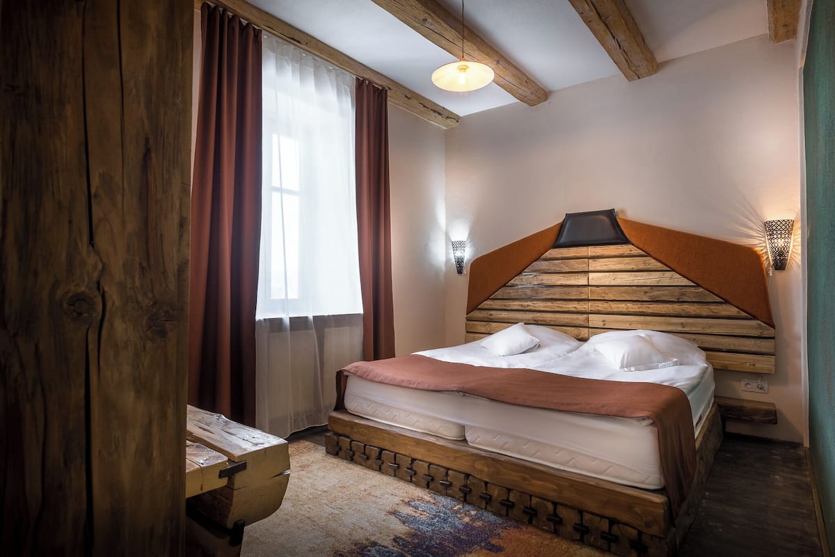 A bedroom with a wooden headboard, a bed with white linens, a small table, and a window with curtains.