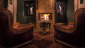 A cozy room with a brick fireplace, leather armchairs, and a small table. - Castle Hotel Daniel (Bradut)