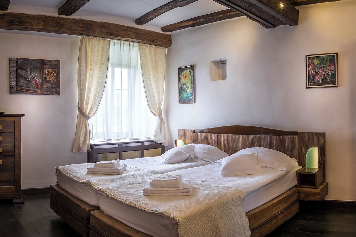 A bedroom with a wooden bed, a nightstand, a dresser, and a window with curtains.