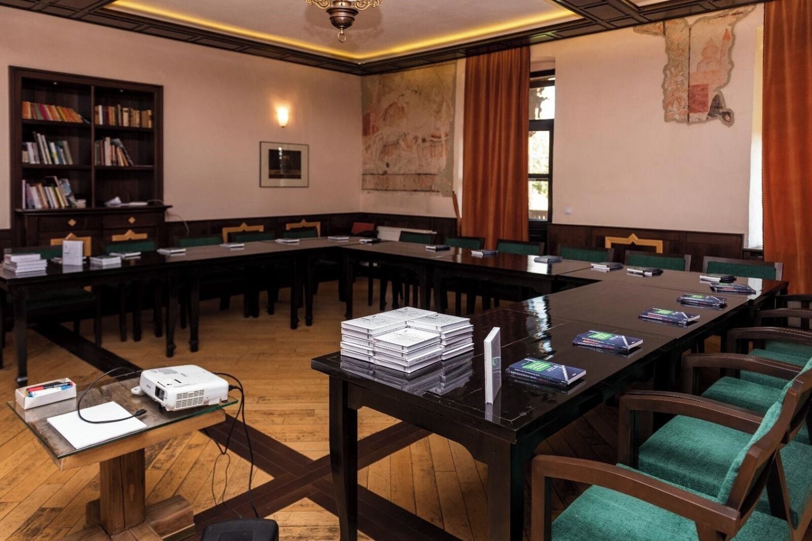 Une salle de conférence avec une longue table, des chaises, un projecteur et des livres.