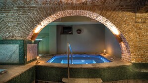 A stone-walled hot tub with a tiled floor, a clock on the wall, and a small window above the tub. - Castle Hotel Daniel (Bradut)