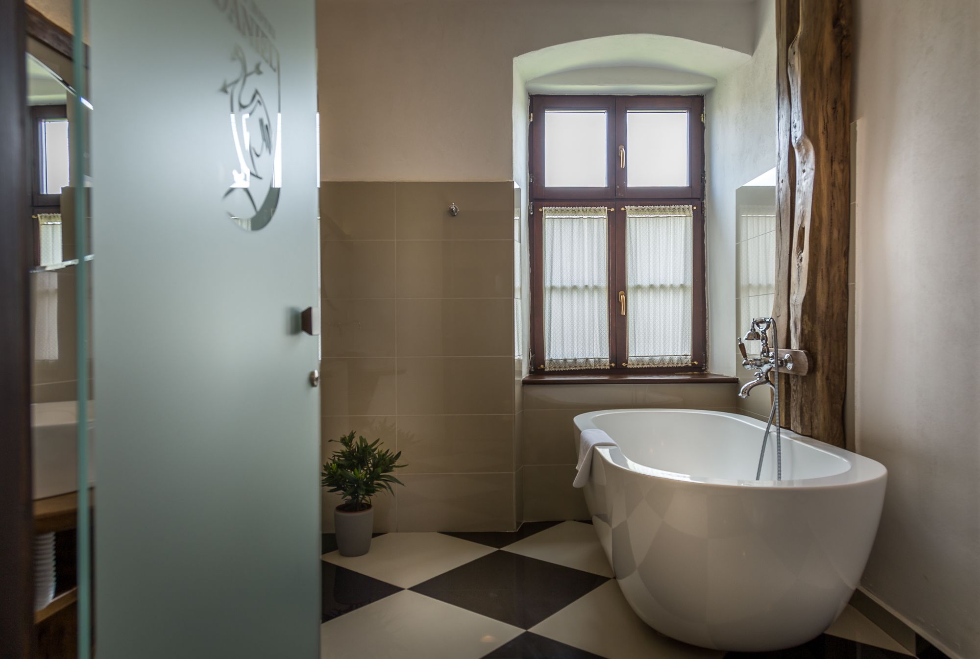 A bathroom with a freestanding bathtub, a window with curtains, and a potted plant.