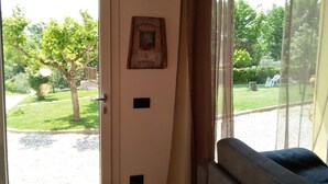 A room with a door leading to a garden, a framed picture on the wall, and a window with curtains. - Il Poggio (Pontedera)