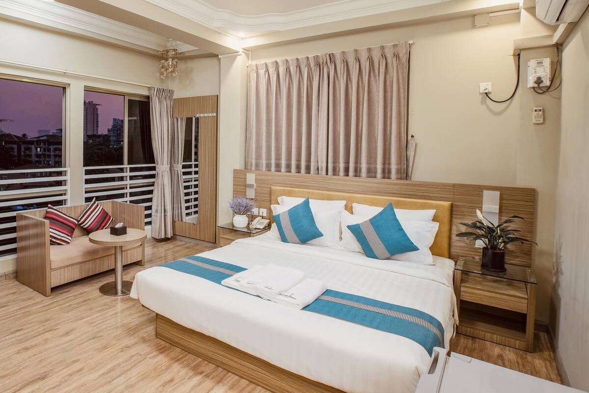 Una habitación de hotel con una cama grande, un sofá, una mesita y una lámpara en la mesita de noche.