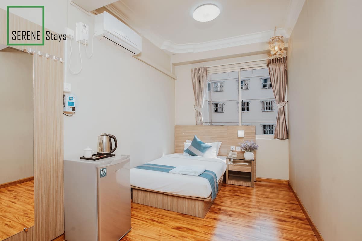 Una habitación de hotel con cama, escritorio, mini refrigerador, ventana con cortinas y aire acondicionado.