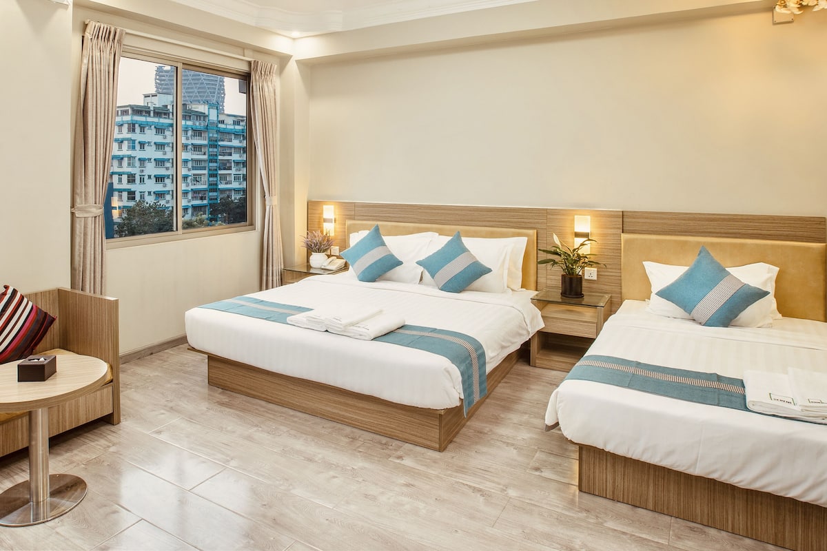 Habitación de hotel con dos camas, un sofá, una mesita y una ventana con cortinas.