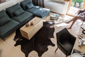 Ein modernes Wohnzimmer mit einem Ecksofa, einem Holztisch, einem Teppich aus schwarzem Leder und einem Ledersessel.
