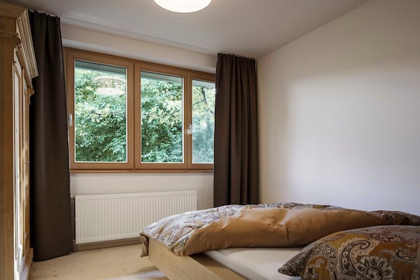 Ein Schlafzimmer mit einem hölzernen Bett, einem Fenster mit Vorhängen und einer Heizung.