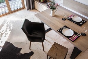 Ein Essbereich mit einem Holztisch, gedeckt für zwei Personen, einem schwarzen Stuhl und einem kleinen Beistelltisch.