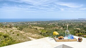 A scenic view of a coastal landscape with a table set with food and drinks. - Villa Ikaros (Rethymno)