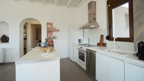 A modern kitchen with white cabinetry, a central island, stainless steel appliances, and a large window. - Villa Ikaros (Rethymno)