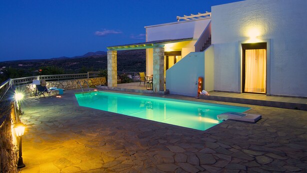 A swimming pool area with stone flooring, a pergola, and a view of mountains in the background. - Villa Ikaros (Rethymno)