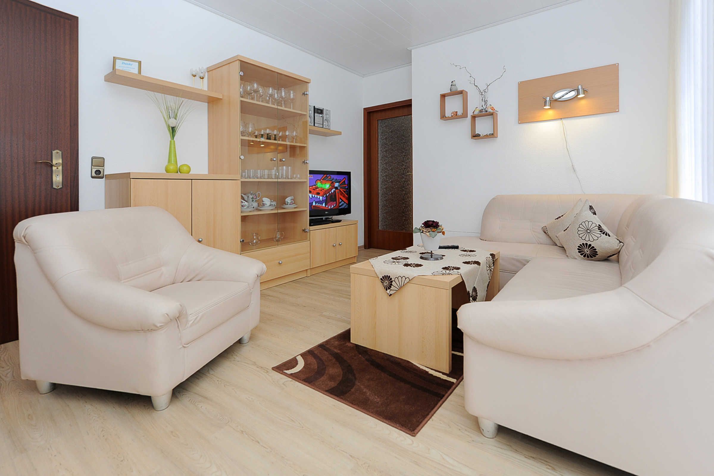 A living room with two white sofas, a coffee table, a wooden cabinet with glassware, a television, and a door with a frosted glass panel.