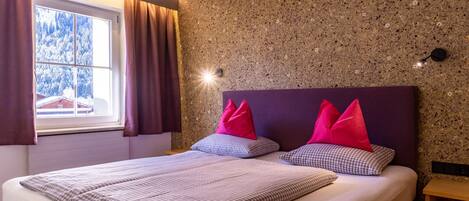 Un dormitorio con cama, ropa de cama a cuadros, ventana con cortinas y pared con textura.