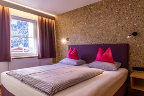A bedroom with a bed, checkered bedding, a window with curtains, and a textured wall.