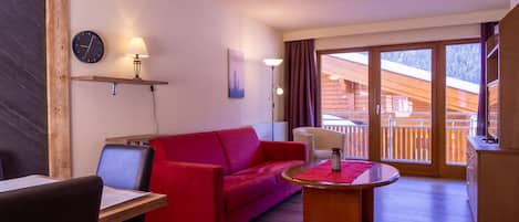 Una habitación acogedora con un sofá rojo, una mesa de madera, una silla, un reloj y una lámpara en un estante.