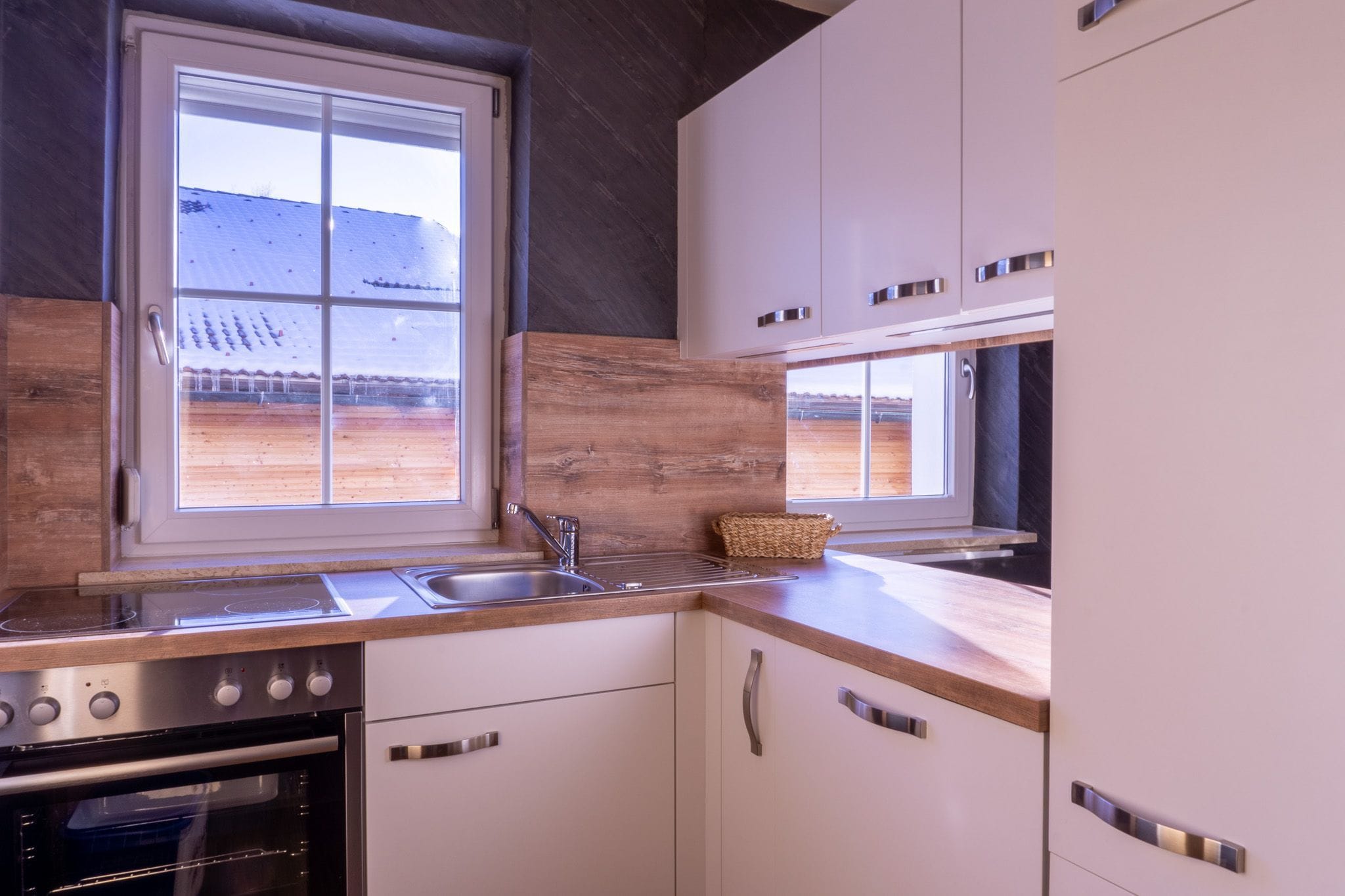 Una cocina moderna con horno empotrado, un lavamanos y una ventana con vista a un paisaje nevado.