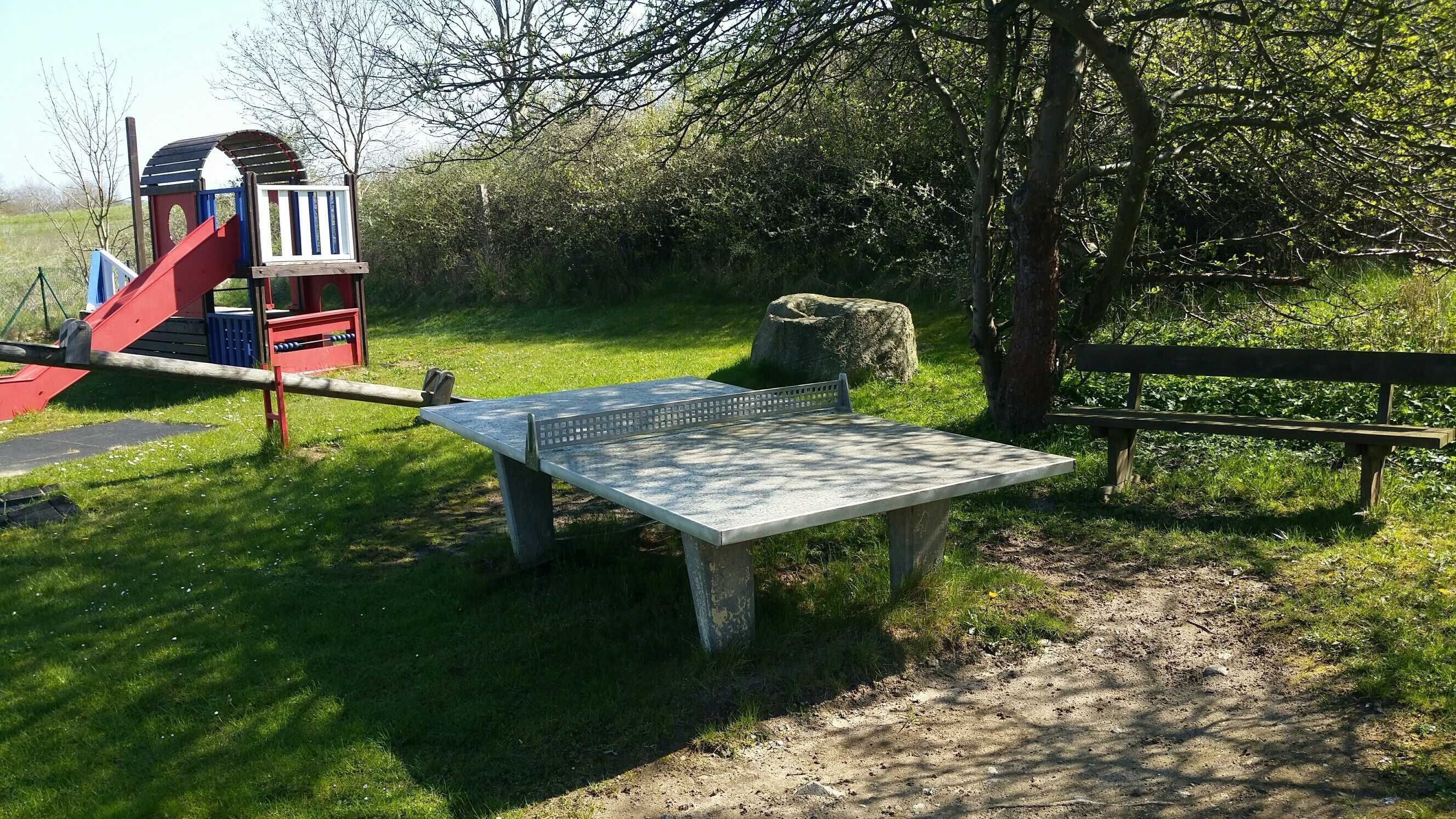 Een speeltuin met een glijbaan en klimconstructie, een betonnen bank en een picknicktafel.