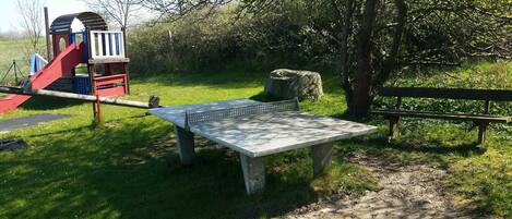 Une aire de jeux avec un toboggan et une structure d’escalade, un banc en béton et une table de pique-nique.