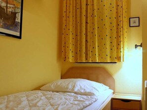A single bed with a wooden headboard, a yellow curtain with a pattern, and a framed picture on the wall.