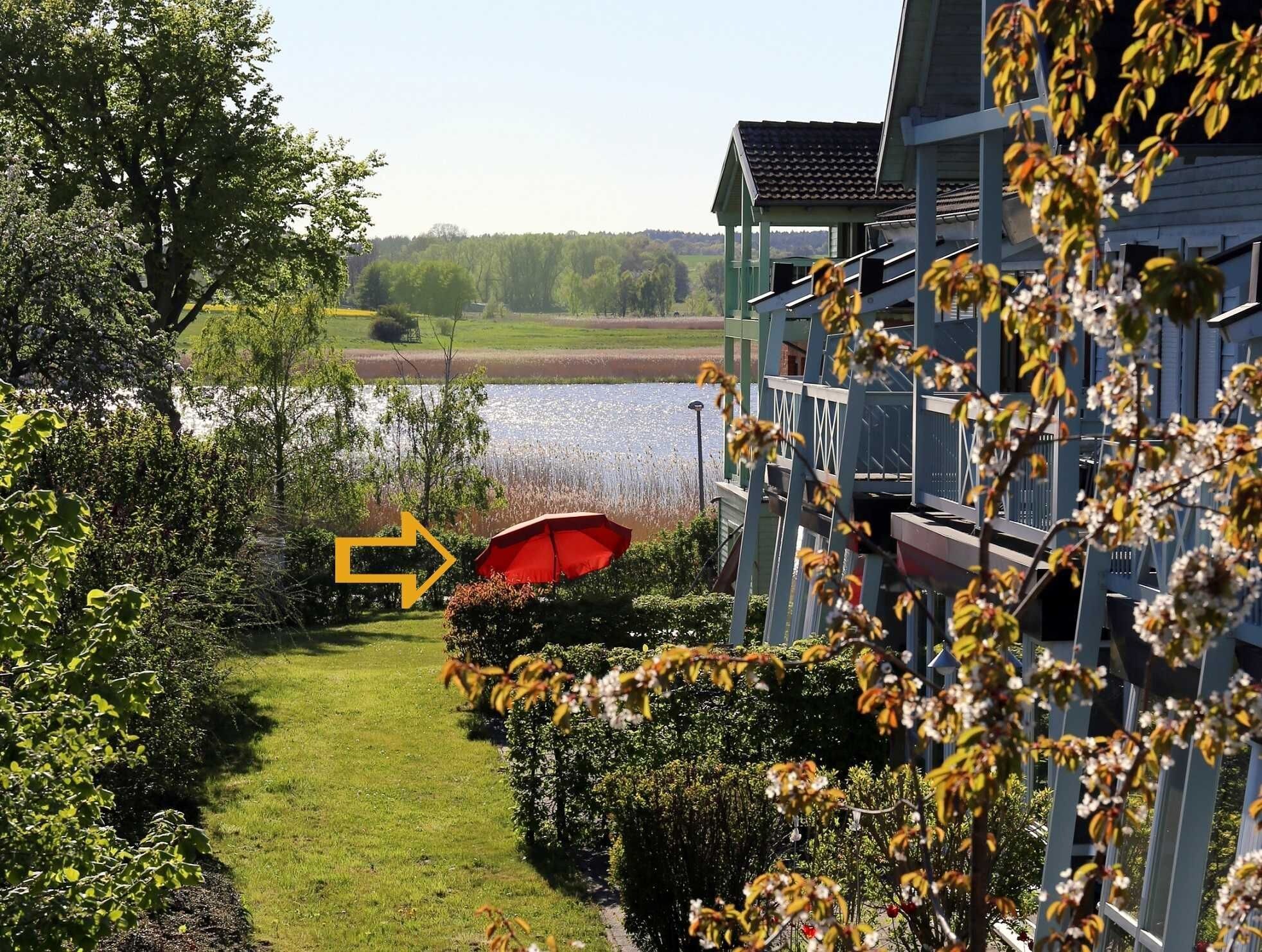A building with a view of a lake, a red umbrella, and a pathway leading to the lake.