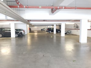 A multi-level parking garage with several cars parked, visible pipes, and a bicycle mounted on the wall.