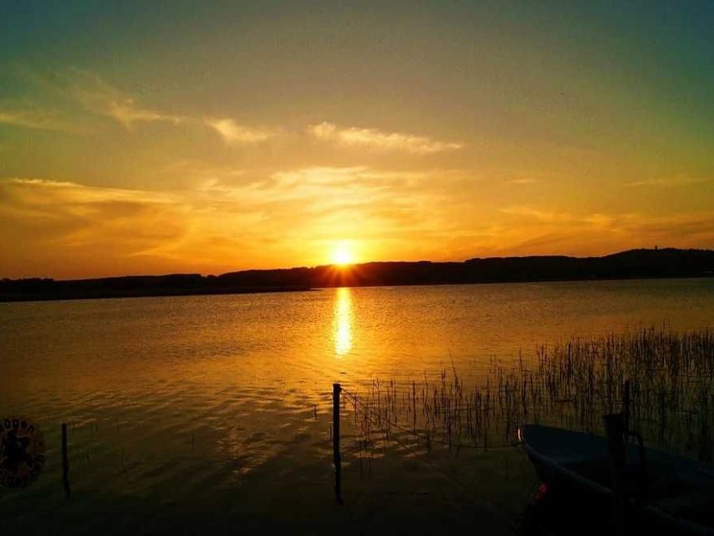 A sunset over a calm body of water with a dock and reeds in the foreground.