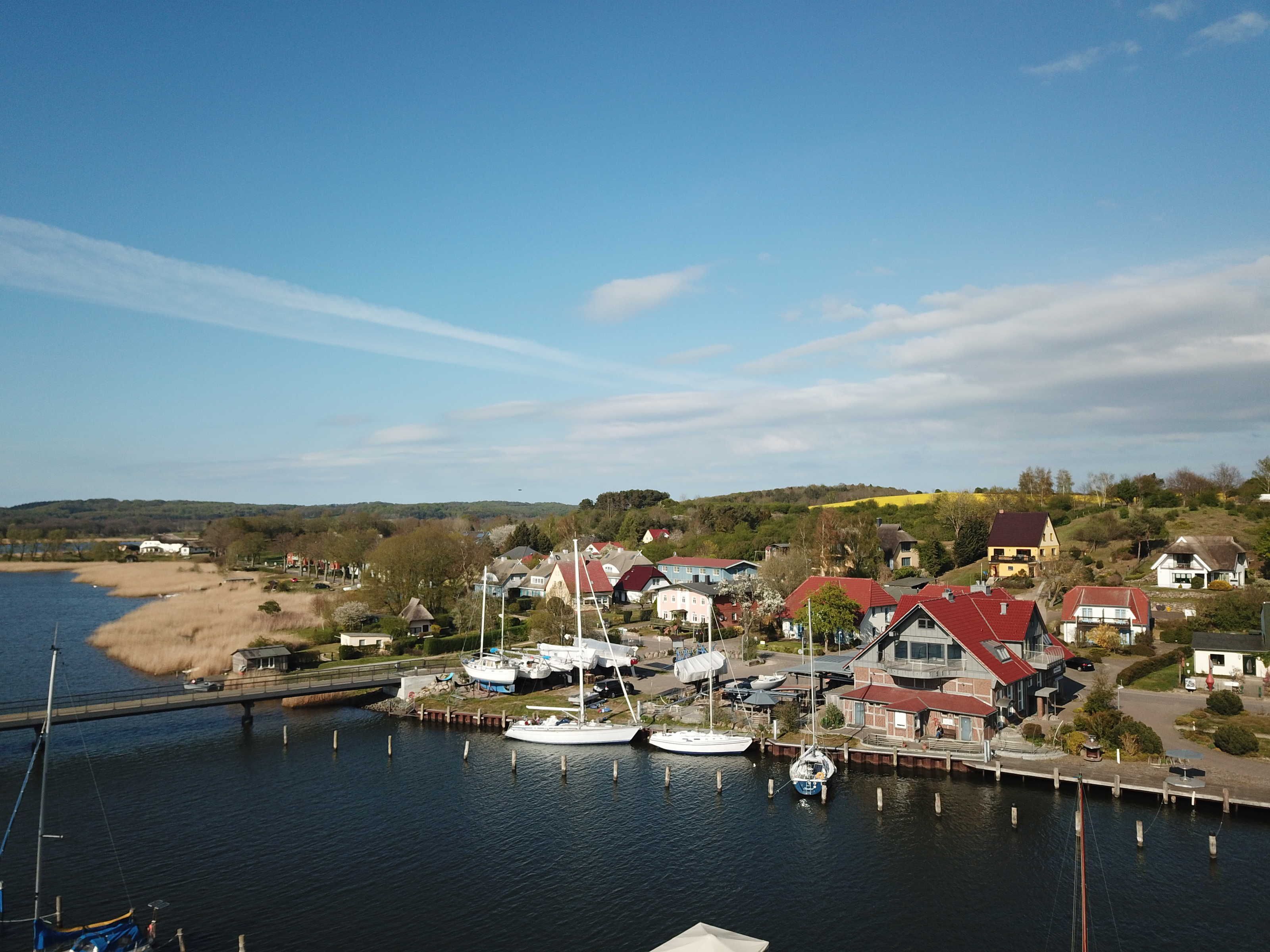 A marina with boats docked, a bridge, and houses with red roofs.