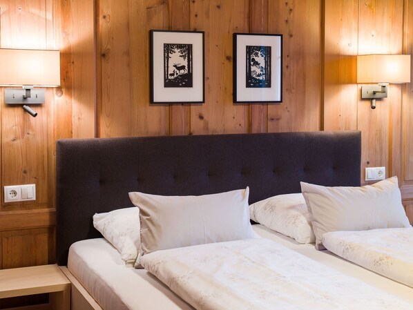 Habitación de hotel con dos camas, cabecero oscuro, obras de arte enmarcadas en la pared y lámparas de noche.