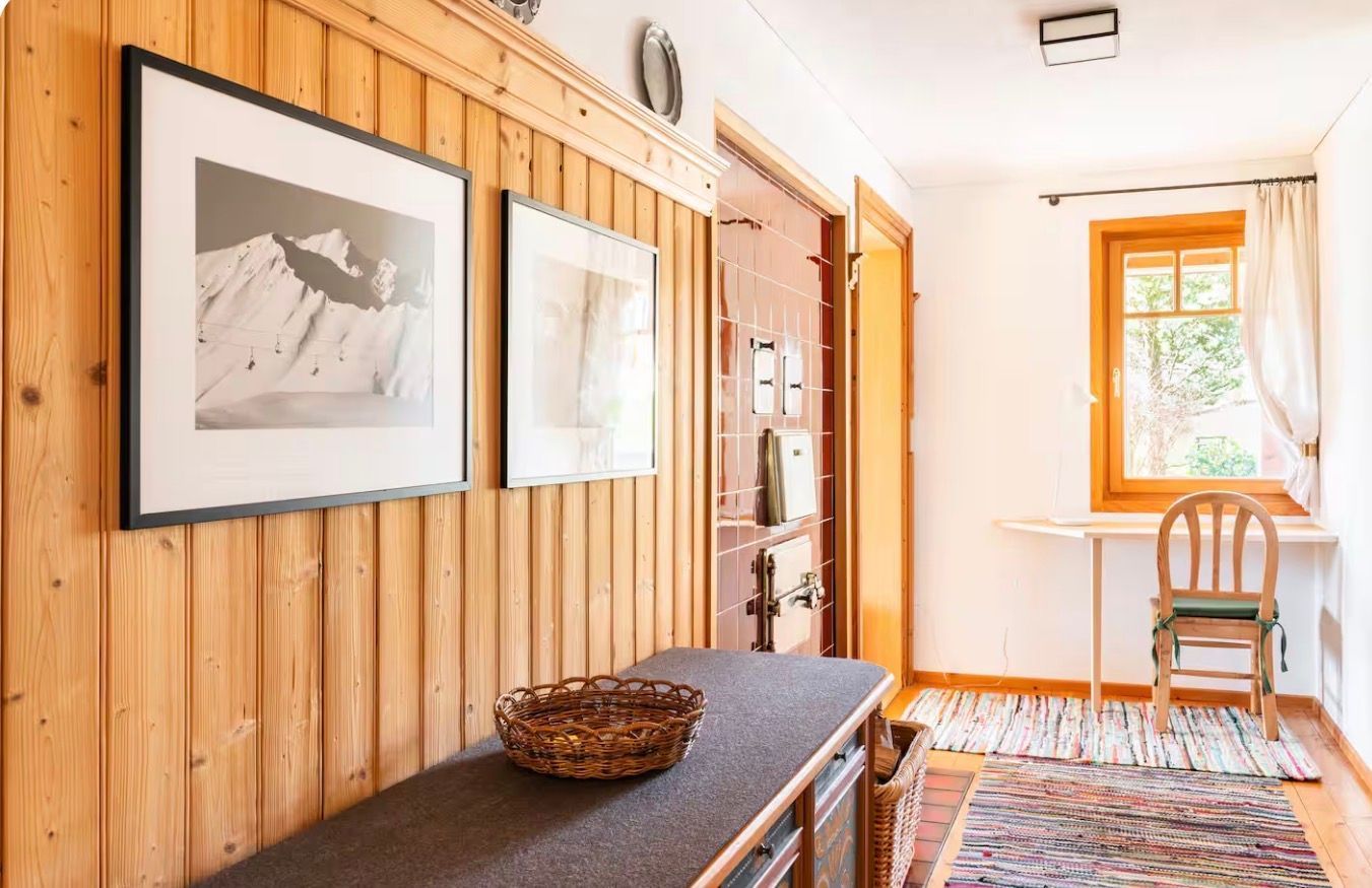 Un couloir aux murs lambrés, avec un banc, un panier et des tableaux encadrés.