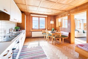 A wooden interior with a kitchen, dining area, and a view through an open door.