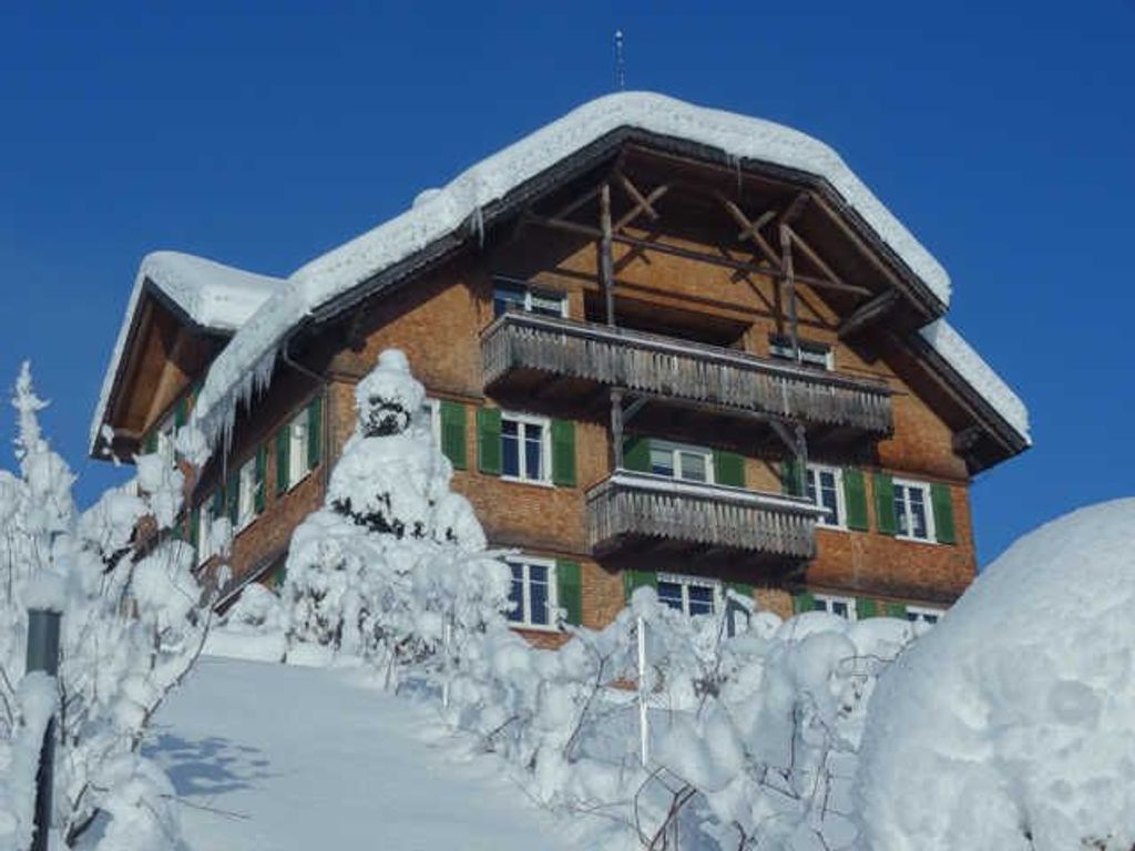 A multi-story chalet with a wooden facade, balconies, and snow-covered surroundings.