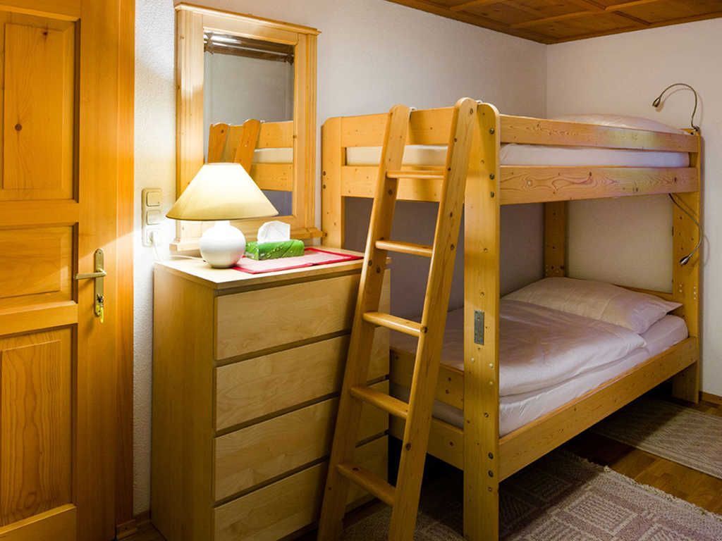 Una cama litera con escalera, un escritorio con lámpara y un espejo.