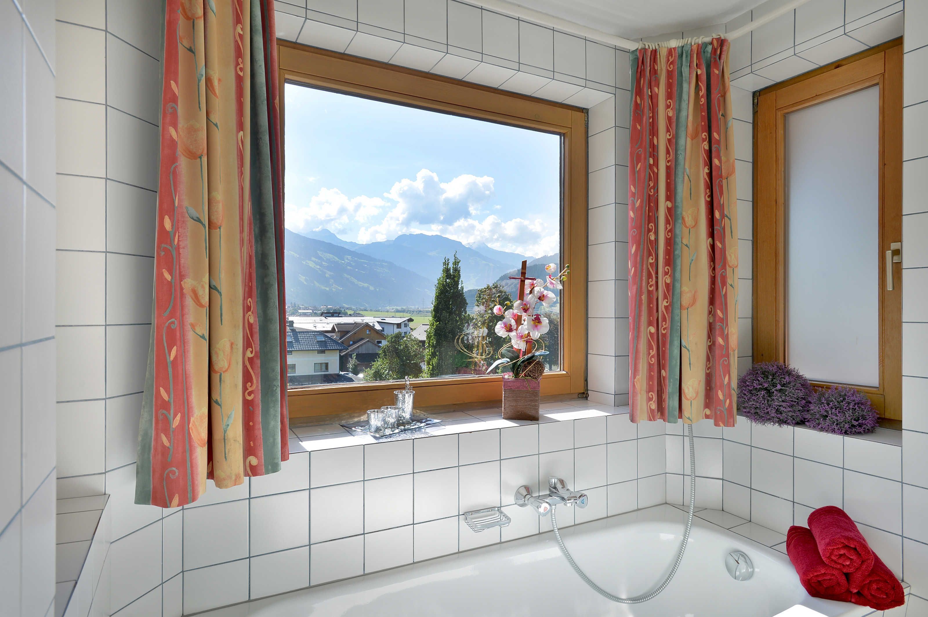 Een badkamer met een raam, een badkuip en een raamzitje met bloemen.