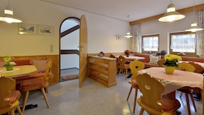 A cozy dining area with wooden furniture, a large open door leading to a balcony, and a window with floral curtains.