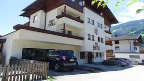 A multi-story building with 'HAUS ZENTRAL' signage, a parking area, and a mountainous backdrop.