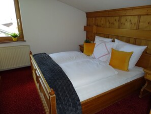 Un letto in legno con biancheria bianca, un tappeto rosso, una finestra con una pianta e una testiera in legno.