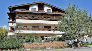A multi-story building with balconies, a stone wall, and a tree in the foreground.