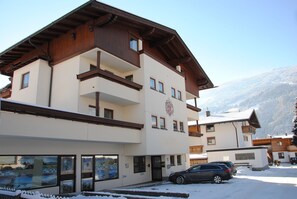 Ein mehrstöckiges Gebäude mit Holzfassade, Balkonen und einem Skigebiet im Hintergrund.
