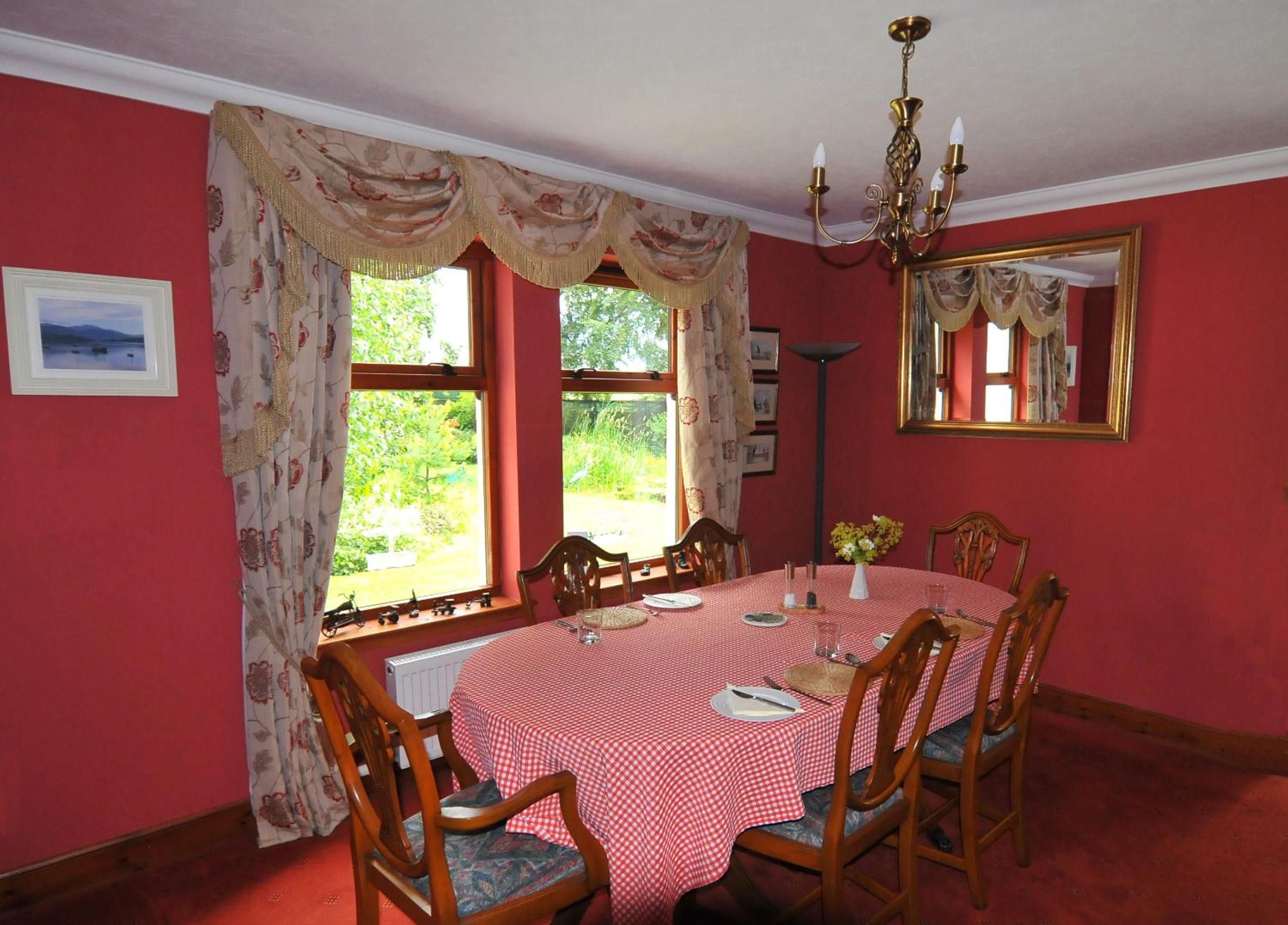 A dining room with a red and white checkered tablecloth, wooden chairs, and a chandelier.