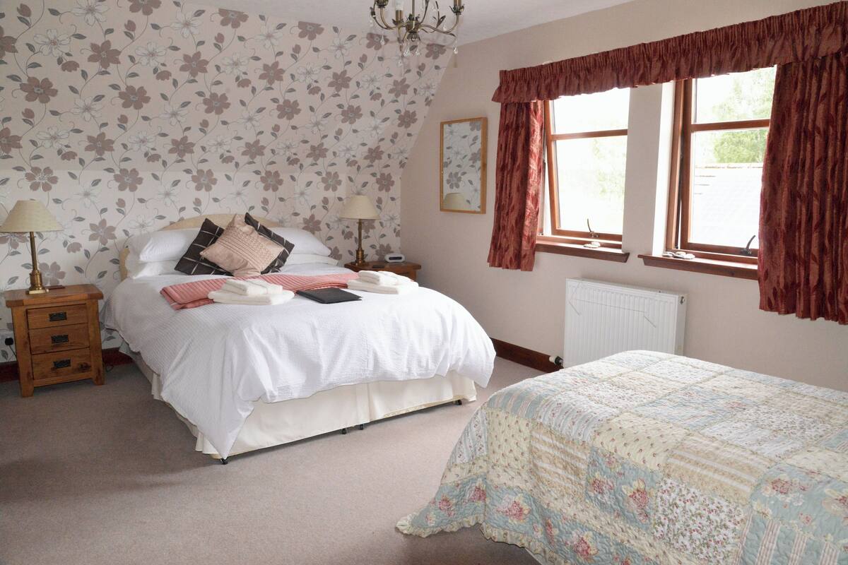 A bedroom with a bed, bedside tables, a nightstand, a window with curtains, and a radiator.