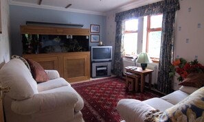 A living room with a sofa, a television, a wooden cabinet, and a window with curtains.