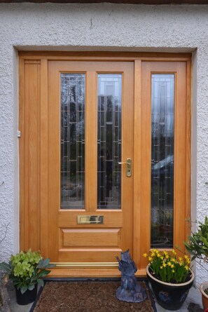 A wooden front door with a glass panel, a mailbox, and two potted plants. - Home Farm (Muir of Ord)