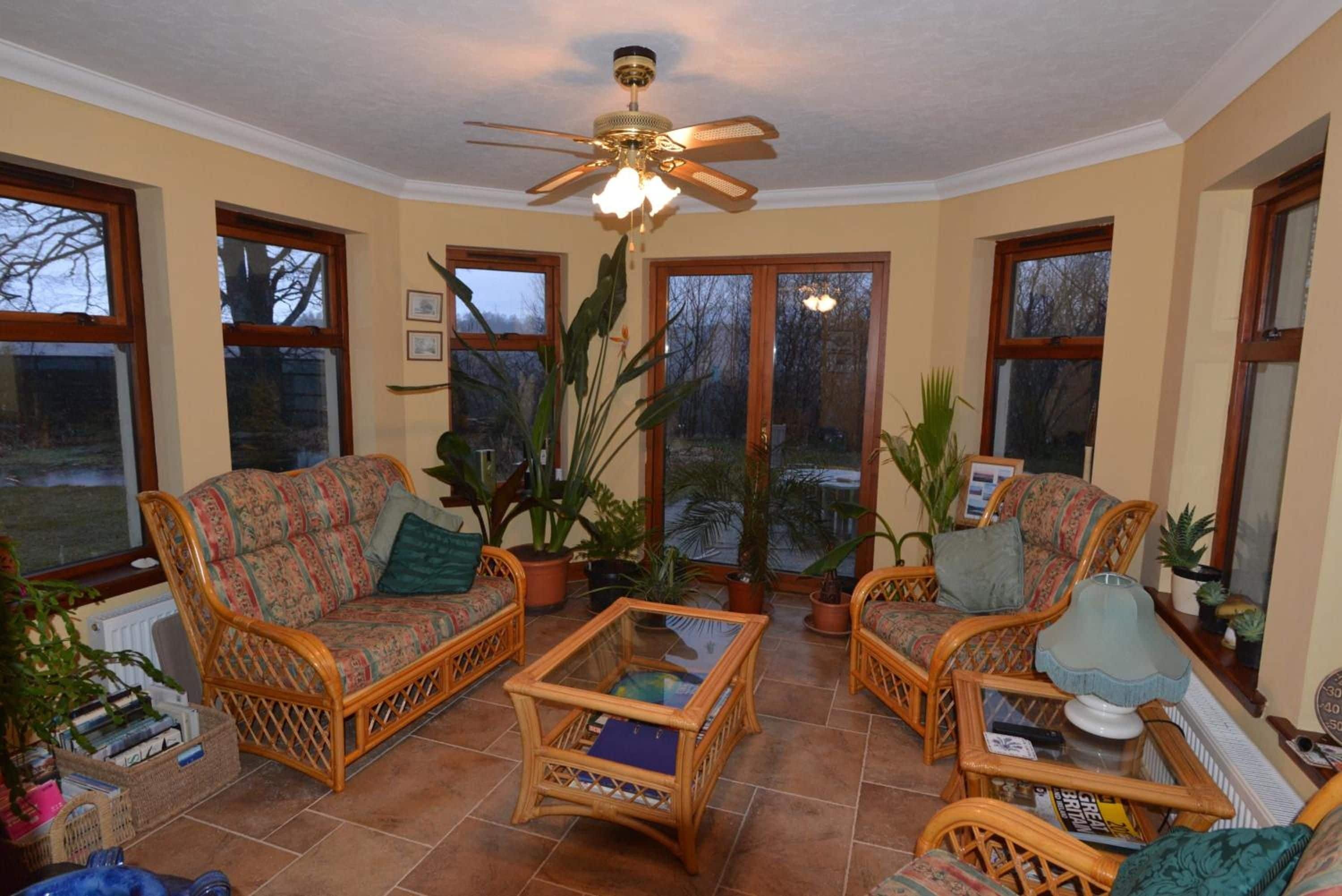 A sunroom with wicker furniture, large windows, and a ceiling fan.