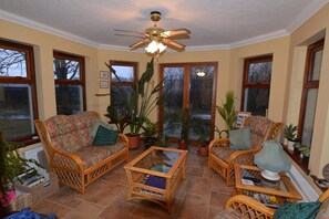 A sunroom with wicker furniture, large windows, and a ceiling fan. - Home Farm (Muir of Ord)